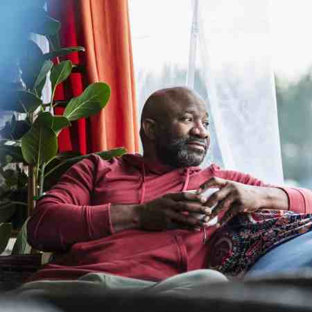 A Black man sits on his sofa, drinking a coffee.