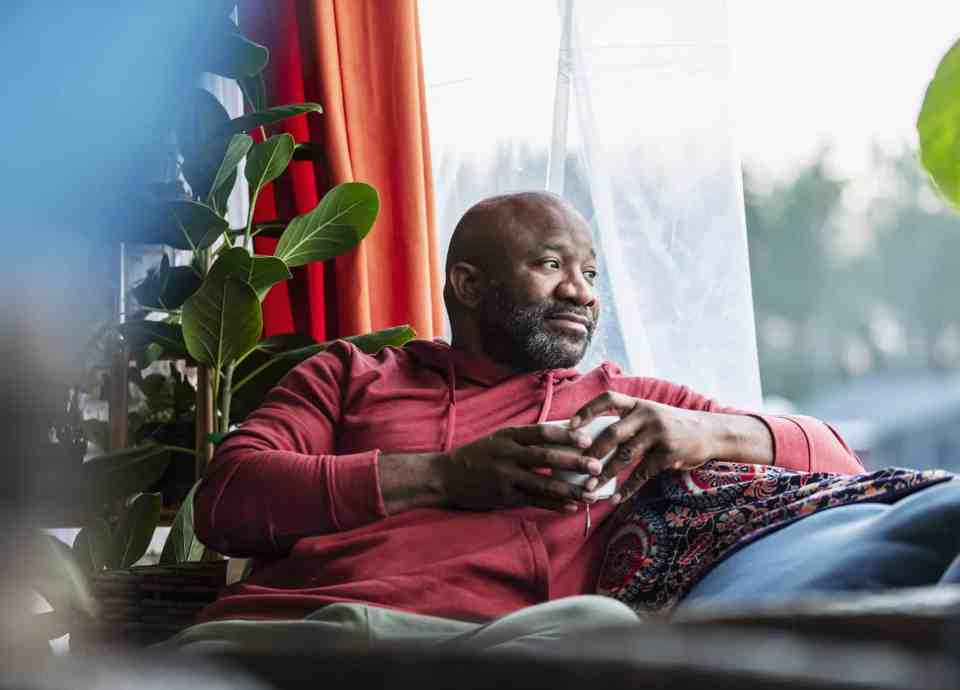 A Black man sits on his sofa, drinking a coffee.