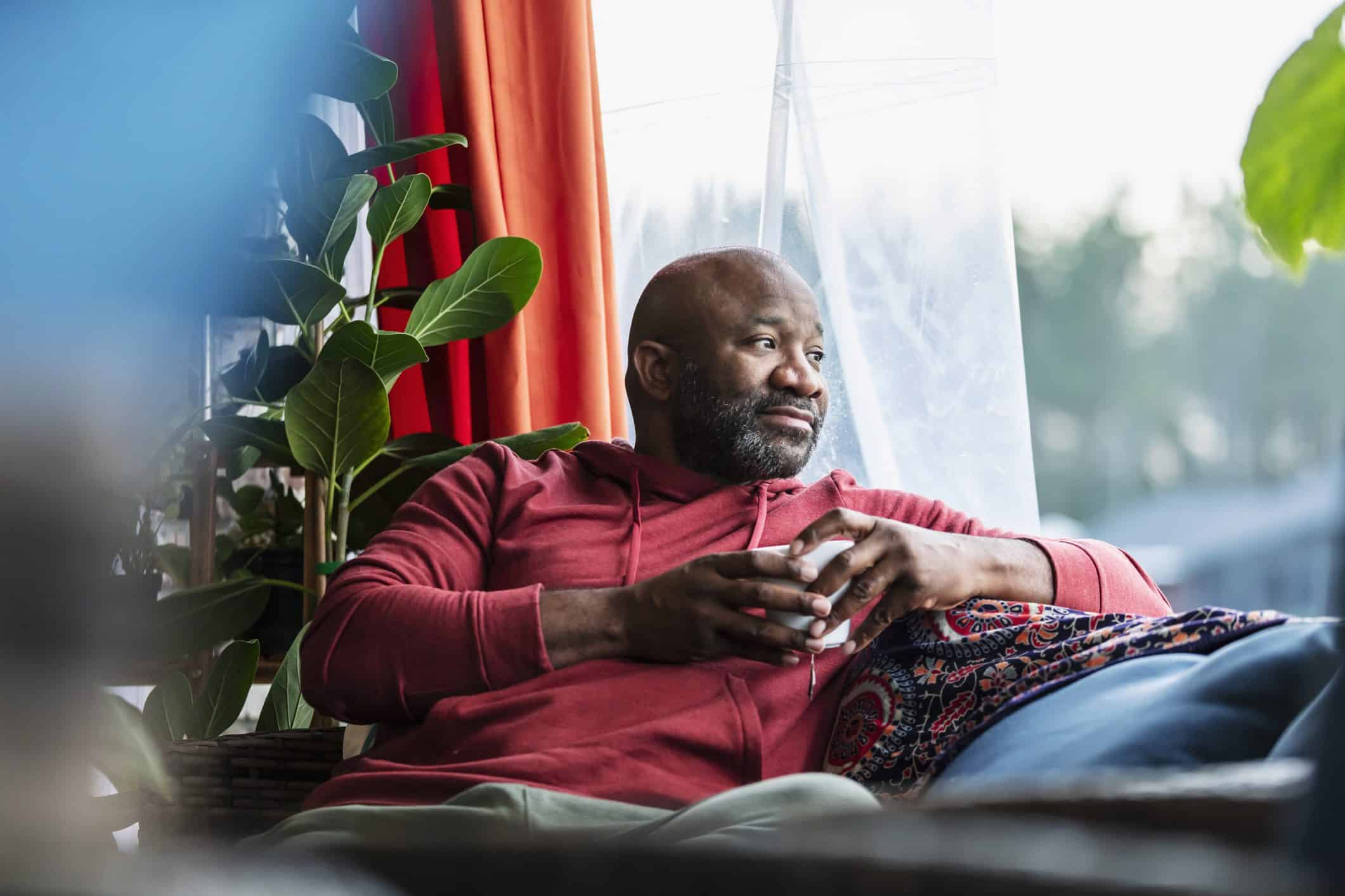 A Black man sits on his sofa, drinking a coffee.