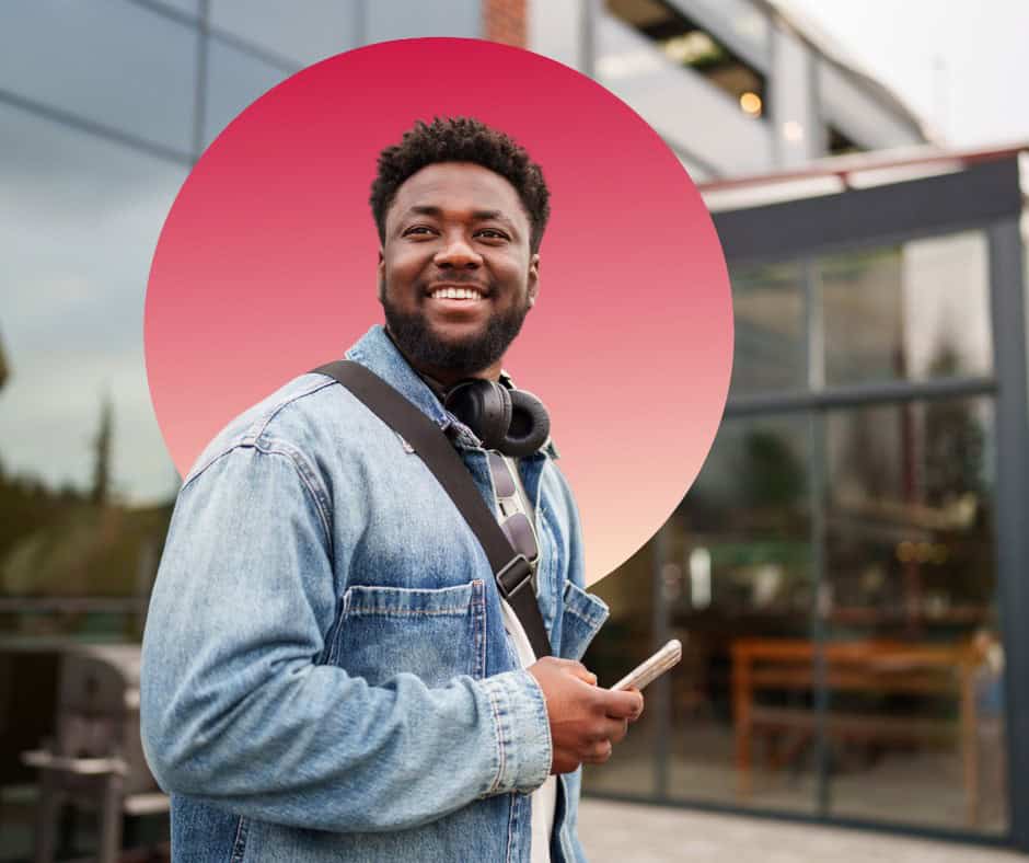 A young man smiling while holding his cell phone.