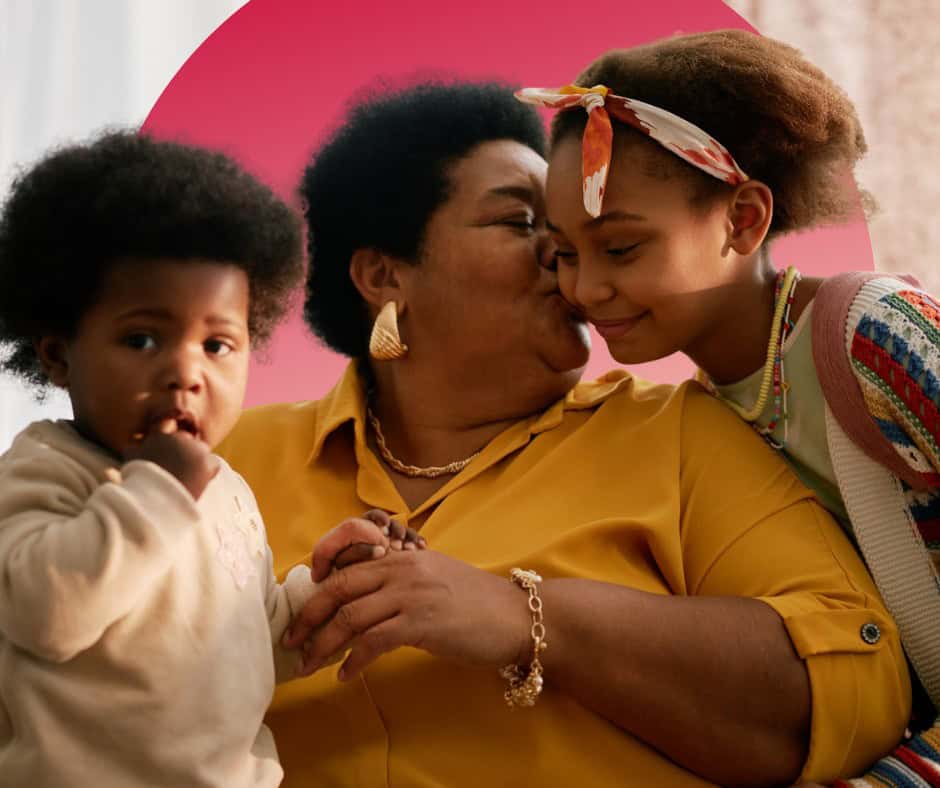 A Black woman snuggles her two grandchildren.